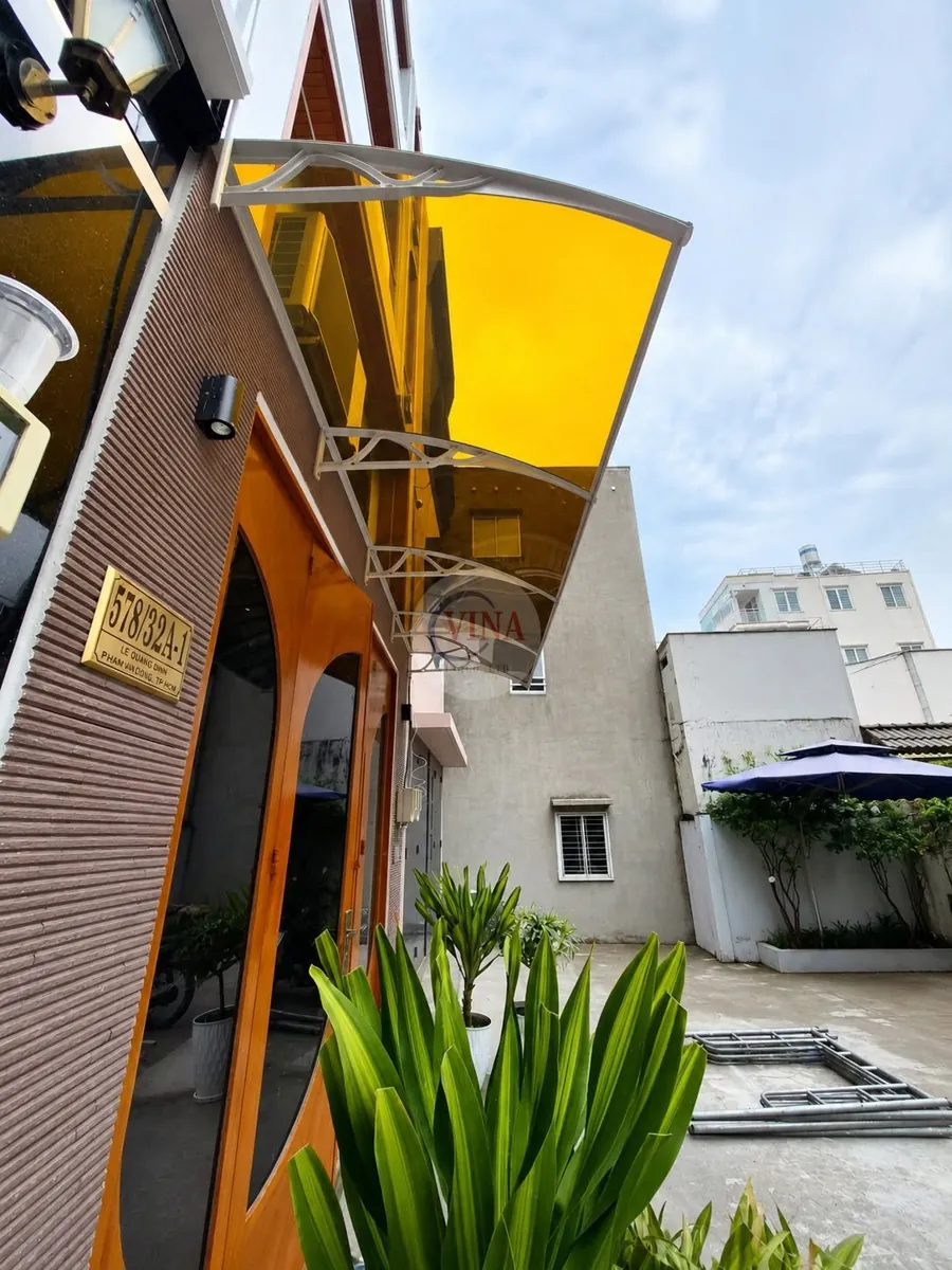 Mái che canopy tấm lợp cản sáng lắp phía trên cửa chính nhà phố, chụp lúc trời nắng gắt ánh vàng hổ phách