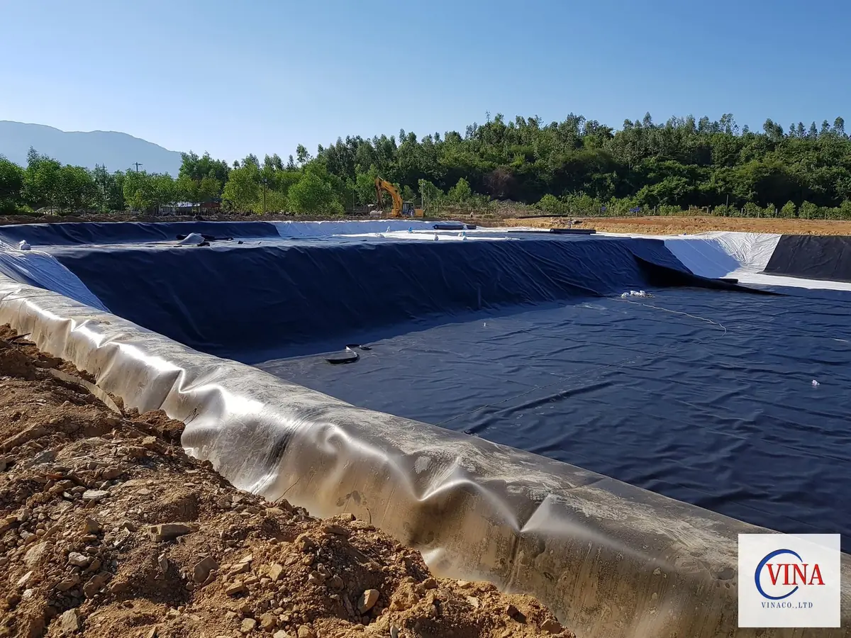 Thi công lót bạt HDPE cho hồ chứa nước tưới tiêu quy mô lớn, có máy xúc và rừng cây bao quanh