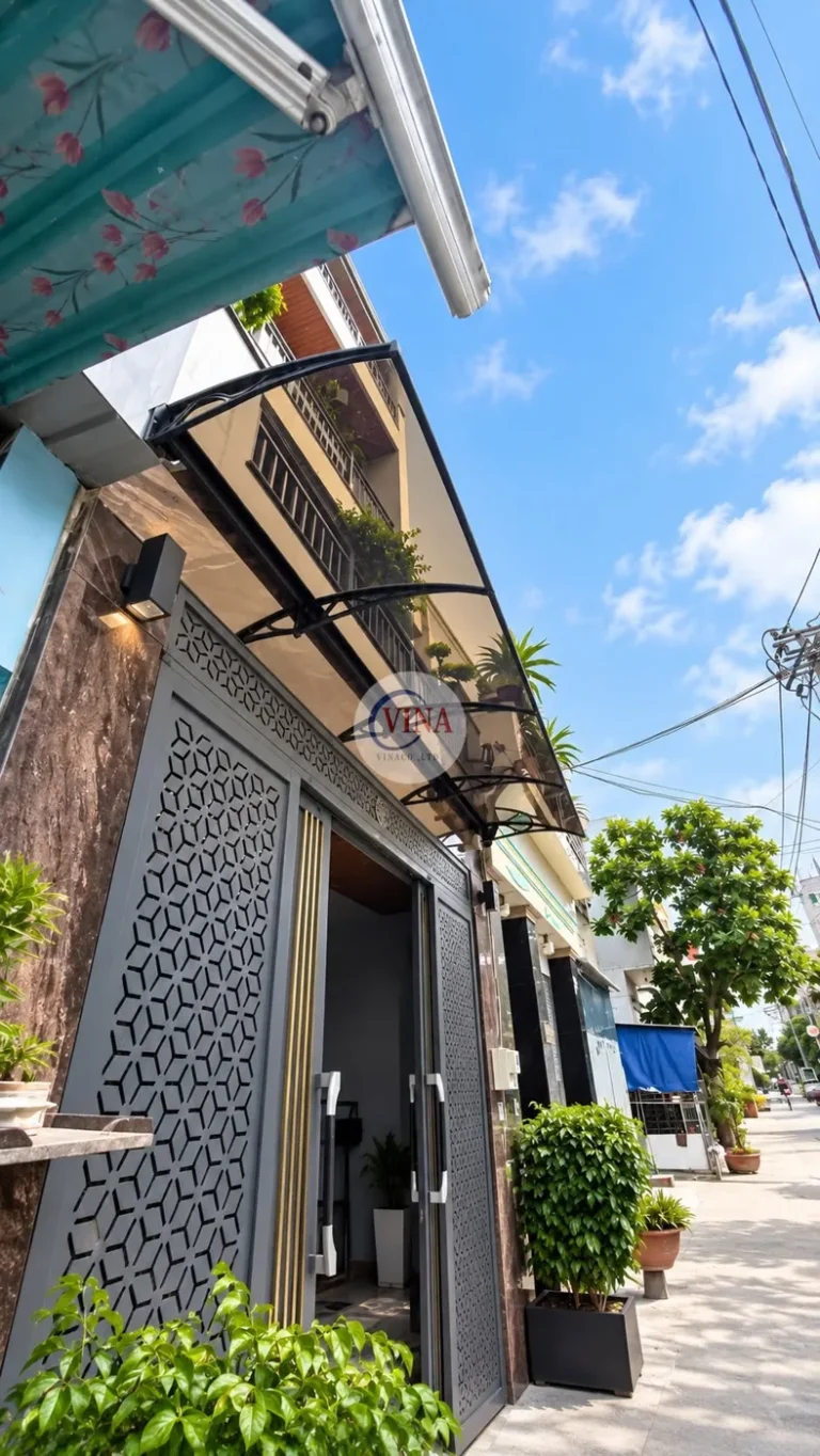 Nhìn từ vỉa hè: mái che vươn ra phía trên lối vào, che cho cửa cổng nhôm hoa văn và khoảng trước cửa.