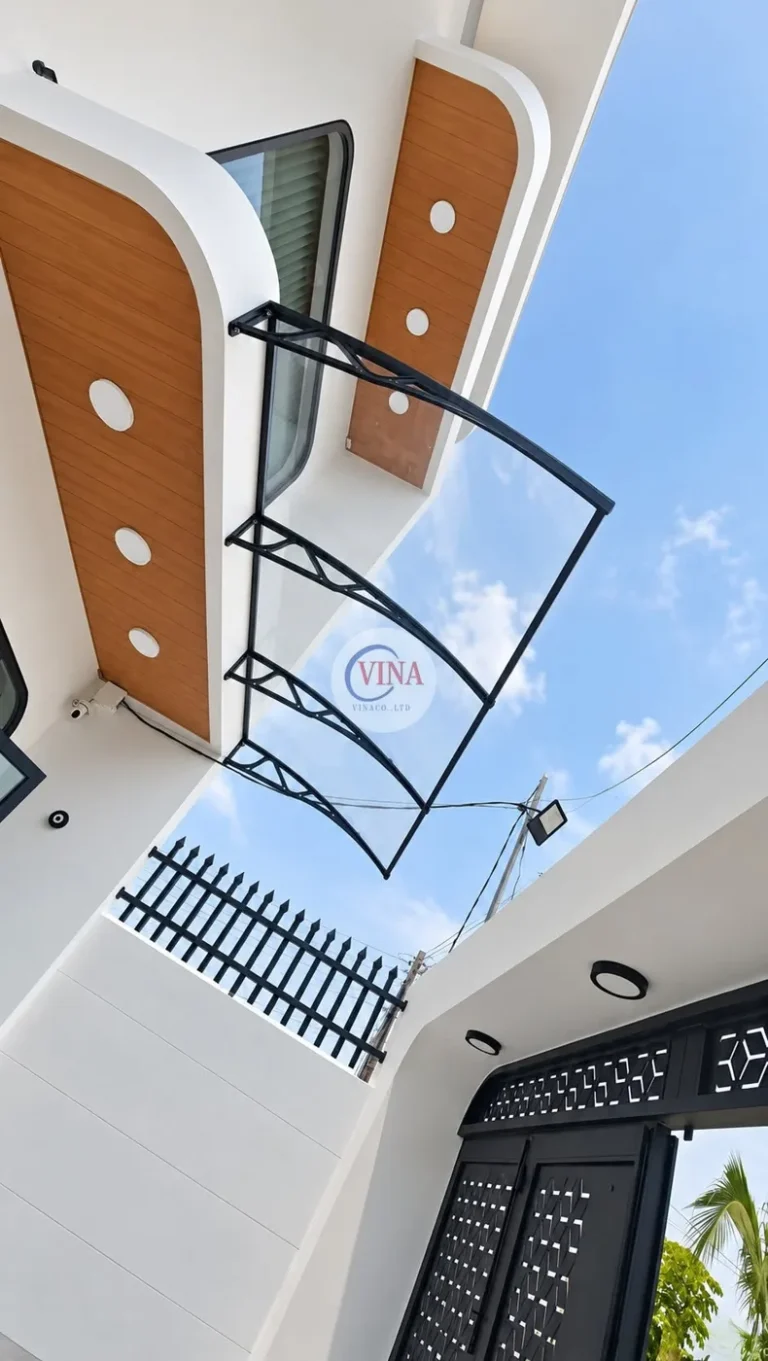Nhìn từ khoảng sân: mái che vươn ra phía hàng rào, ngay trên lối vào gần cổng sắt hoa văn màu đen.