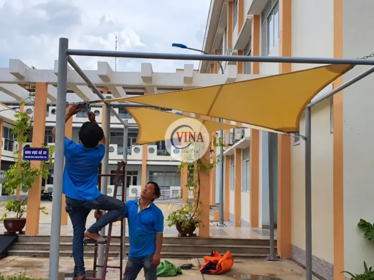 Thợ đang chỉnh phần neo của tấm bạt vàng trên thang.