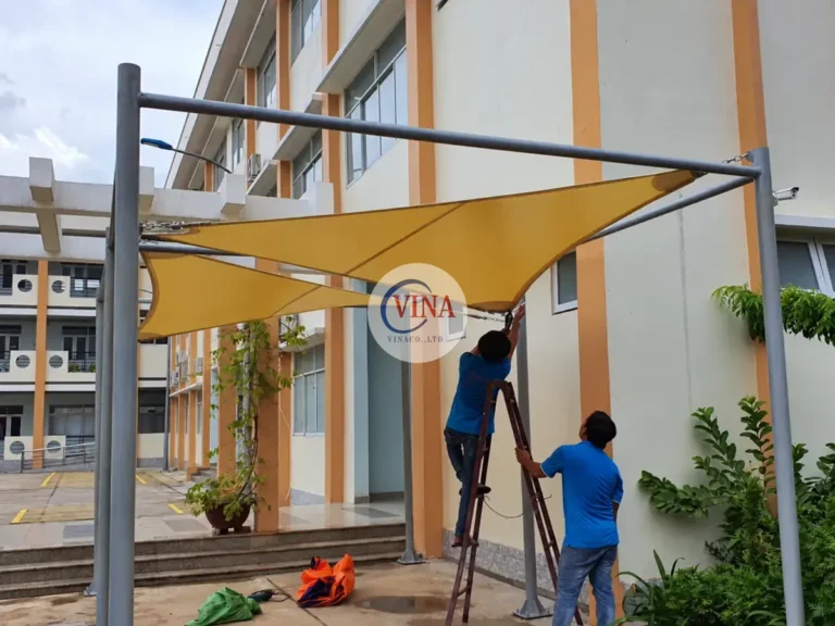 Hai thợ đang hoàn thiện mái bạt vàng sát lối đi bên cạnh tòa nhà.