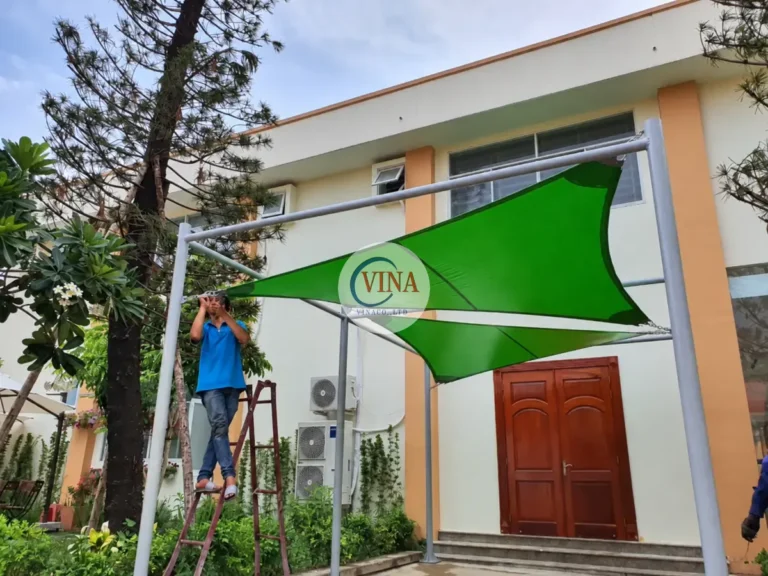 Thợ thao tác ở mép mái bạt xanh phía trước cửa lớp học.