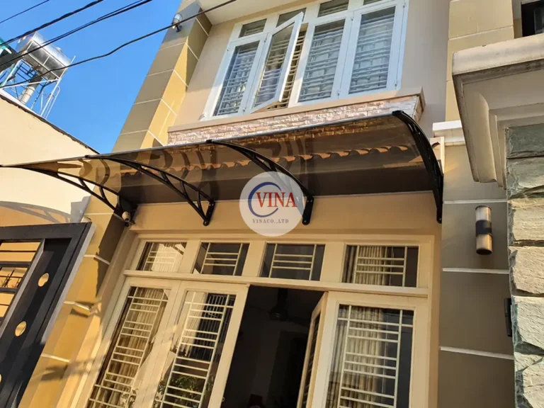 Tấm mái nâu trà đón ánh sáng phía trên cửa và trụ cổng màu xám.