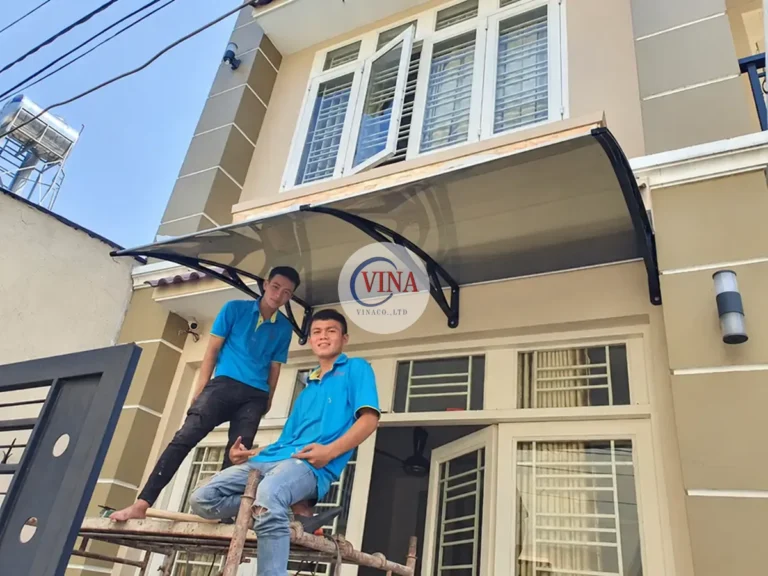 Hai thợ đang hoàn thiện phần mái phía trên cửa, với thang đặt sát tường.