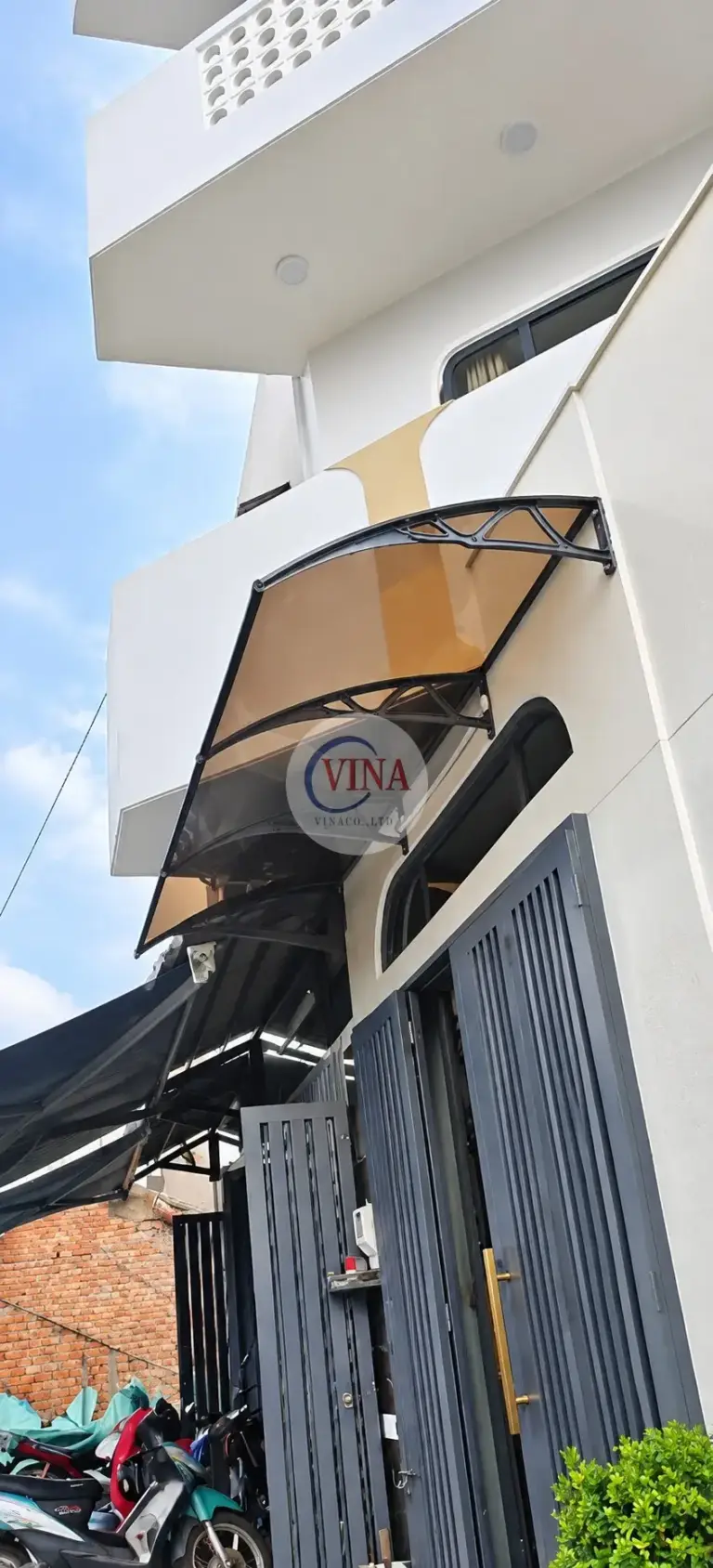 Chụp từ trong hẻm: mái nằm gọn dưới ban công gạch bông gió, phía trên bộ cửa nan dọc.