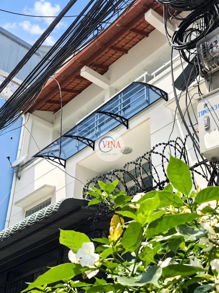 Ở căn nhà phố: mái che chạy dọc lan can ban công, đỡ bằng ba tay đỡ màu đen chia đều.
