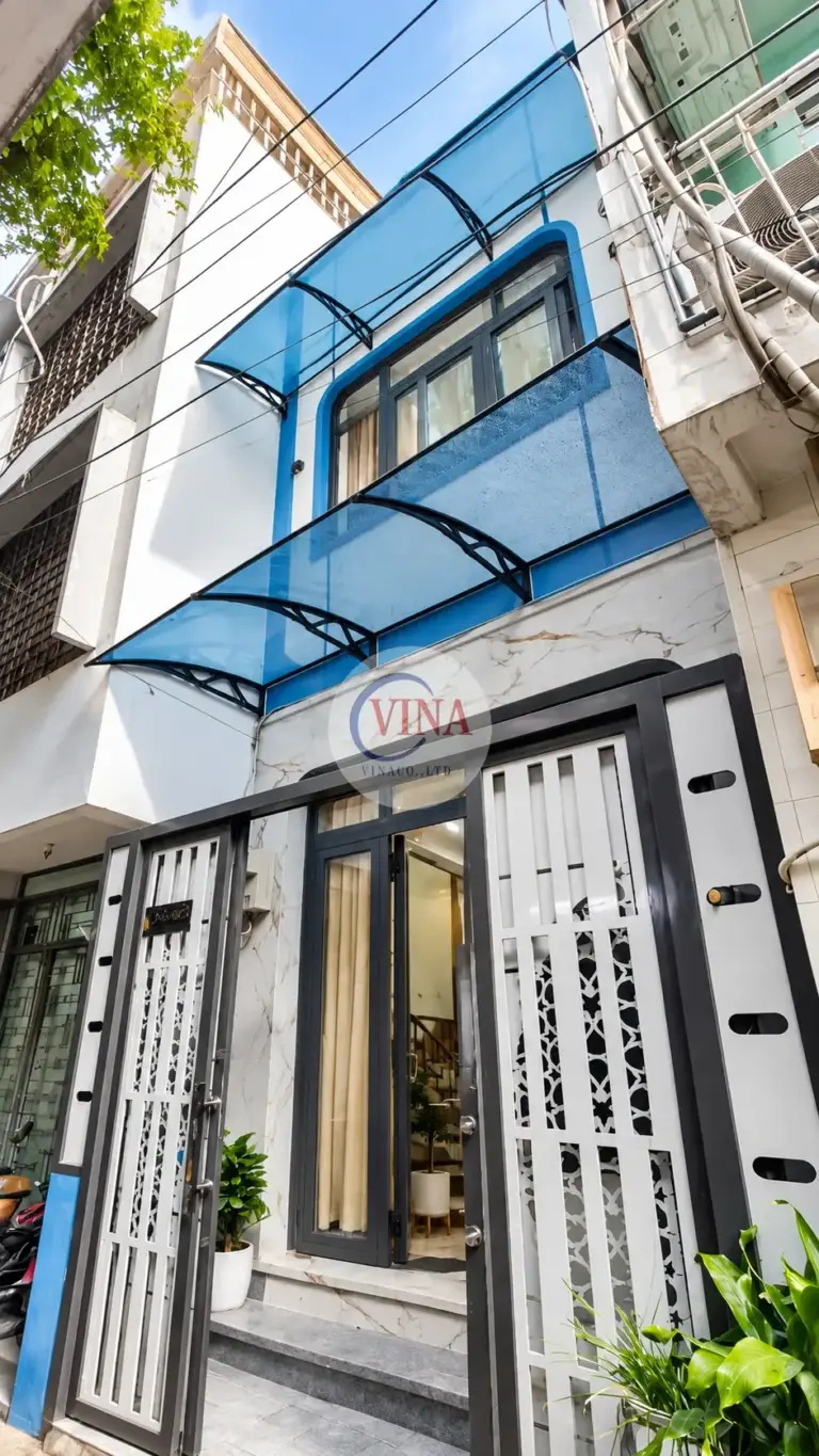 Nhìn từ góc hẻm: mái xanh dương nằm trên dải tường xanh, phía dưới là cổng sắt xám đen ô trắng hoa văn.