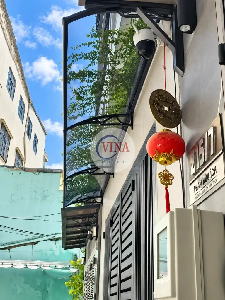 Nhìn từ dưới lên: tay đỡ đen dạng vòm có lỗ hoa văn, tấm xám khói vẫn cho thấy rõ bầu trời và cây xanh phía sau.