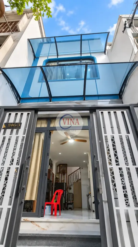 Chụp thẳng từ hẻm: mái xanh dương trên cổng và lớp mái xanh nhạt phía trên cửa sổ tầng lầu.